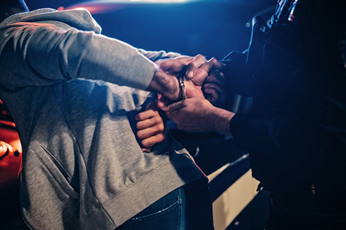 A person in a grey hoodie is being handcuffed by law enforcement officers.
