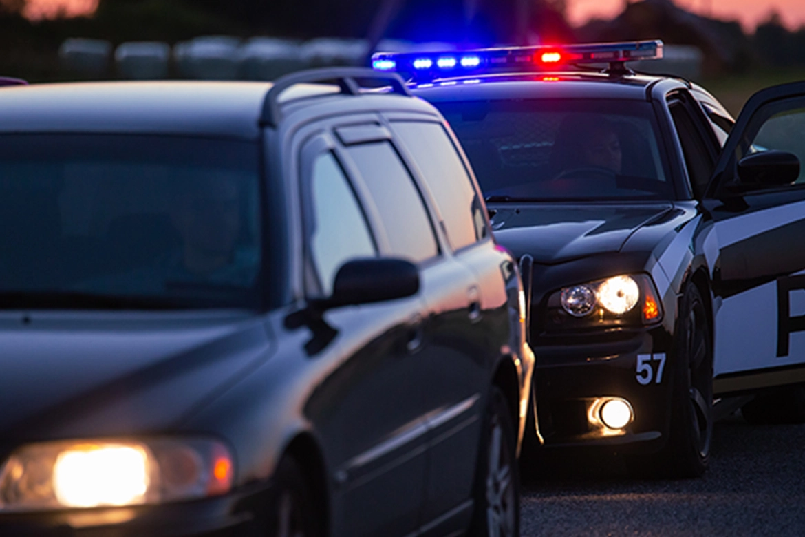 A police car with its lights flashing (red and blue) positioned behind another dark-colored vehicle.