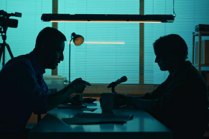shot of an offender, perpetrator or prisoner sitting in the interrogation room in front of the detective